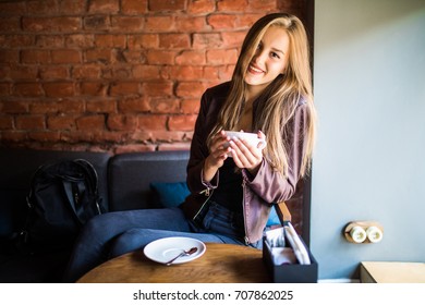 Young Attractive Woman Has A Coffee Break, Sitting In Cafe With Beautiful Interior And Enjoying The Moment