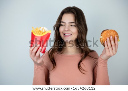 young attractive woman holding meat burger in one hand and fried potatoes in another on isolated white background dietology and nutrition