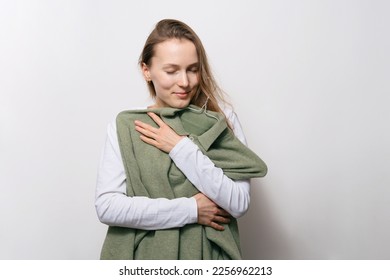 Young attractive woman hugging her favorite winter woolen sweater on white isolated background. Concept of changing wardrobe and favorite clothes
