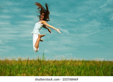 Young attractive woman jumping in sky, against green of summer park.