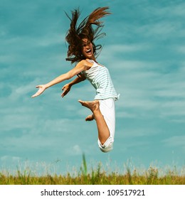 Young attractive woman jumping in sky, against green of summer park.
