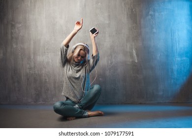 Young and attractive woman listening to music in the mobile app. Girl music lover. Grey clothing and background - Shutterstock ID 1079177591