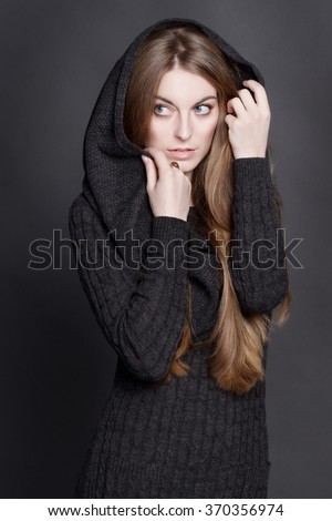 Young attractive woman with long, gorgeous dark blond hair. She is dressed in warm gray knit dress with a hood. She is concerned. She looks around and hides her face.