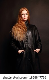 Young attractive Woman with long red hair in a black coat.Girl with long hair on a dark background. Model with in a black leather coat.Leather clothes.Portrait of attractive young Woman with red lips 