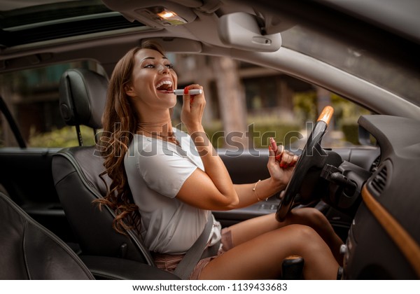 Young attractive\
woman looking in rear view mirror painting her lips doing applying\
make up in the car.\
