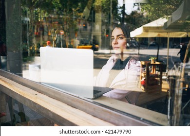 Young Attractive Woman Is Making Plans For The Future, Sitting In Front Of An Open Laptop Computer In A Cozy Coffee Shop.Modern Young Business Woman Thinking About A New Project,looking At The Window.