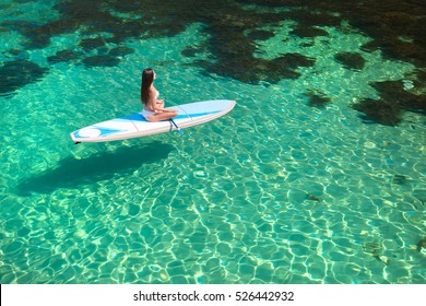 Young attractive woman meditating on the sup board in the sea. Girl in meditative pose on water.