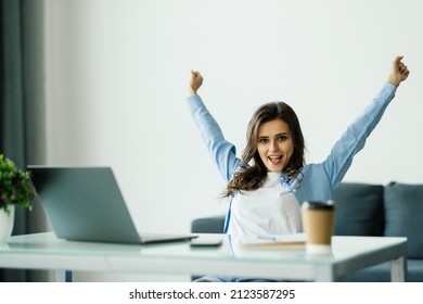 Young attractive woman at a modern office desk, with laptop, stretching her arms with extreme joy special prize winner, office holiday party, found a job, got a date invitation, end of the working day - Shutterstock ID 2123587295