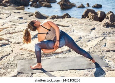 Young attractive woman practices yoga in the bound side angle pose on the beach. Healthy lifestyle concept. - Powered by Shutterstock