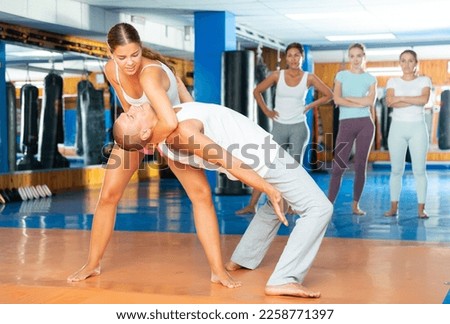 Young attractive woman is practicing self-defence moves in pair with her trainer at gym