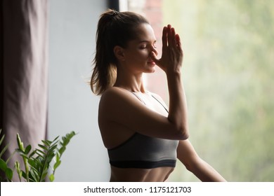 Young Attractive Woman Practicing Yoga, Doing Alternate Nostril Breathing Exercise, Nadi Shodhana Pranayama Pose, Working Out, Wearing Sportswear, Grey Top, Indoor Close Up, Yoga Studio, Side View