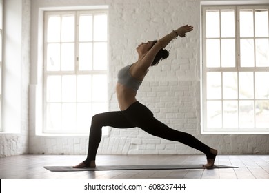 Young attractive woman practicing yoga, standing in Warrior one exercise, Virabhadrasana I pose, working out, wearing sportswear, full length, white studio background, side view. Weight loss concept