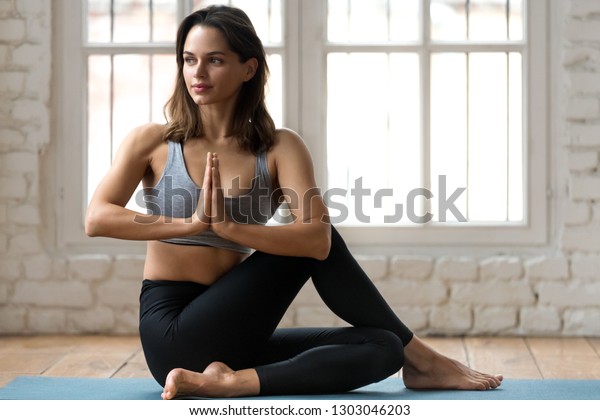 Молодая привлекательная женщина, практикующая йогу, делает Половина лорда рыб упражнения, Арда Matsyendrasana позы с намасте, тренировки, носить спортивную одежду, брюки и топ, крытый полный длины, студия йоги