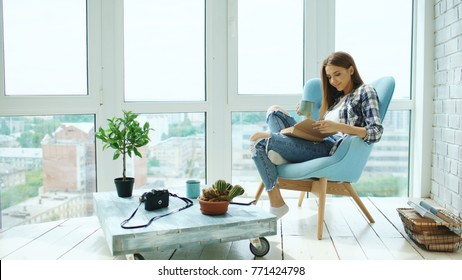 Young attractive woman read book and drink coffee sitting on balcony in modern loft apartment