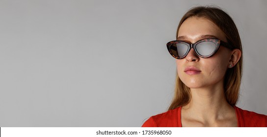 Young attractive woman in red on gray background. Portrait of young woman. Woman posing with sunglasses. Scar on face.
