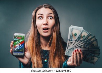 Young Attractive Woman Showing Sincere Excitement About Victory In Online Lottery. Girl Being Happy Winning A Bet In Online Sport Gambling Application On Her Mobile Phone. 