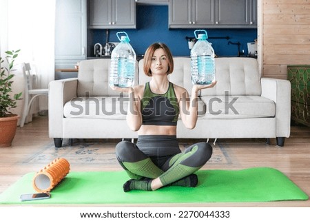 Young and attractive woman in sportswear training at home with five litres water bottles
