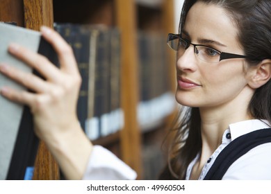 Young Attractive Woman Standing At Book Shelf In Old Library Pulling Out A Book.