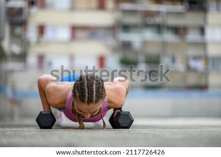 Young attractive woman training outside while using dumbbells and airpods