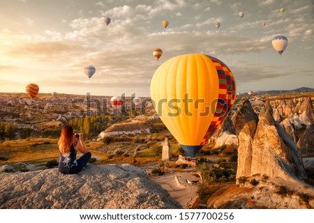 Young attractive woman watches and photographs flying colorful balloons on an early morning in Goreme Valley, Cappadocia. Turkey.
Cappadocia one of the best places to fly with hot air balloons. 