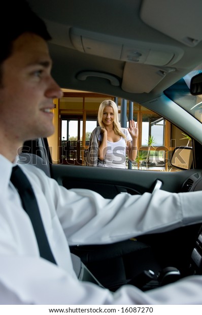A young attractive woman waves goodbye to her\
husband driving to work