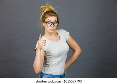 Young Attractive Woman Wearing Eyeglasses Pointing Into Camera, Teenage Judging Someone. Studio Shot On Grey Background.