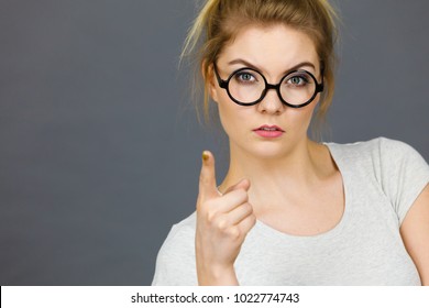 Young Attractive Woman Wearing Eyeglasses Pointing Into Camera, Teenage Judging Someone. Studio Shot On Grey Background.