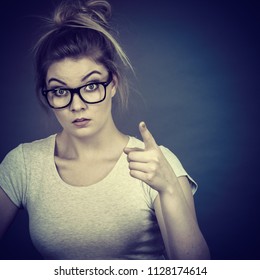 Young Attractive Woman Wearing Eyeglasses Pointing Into Camera, Teenage Judging Someone. Studio Shot On Grey Background.