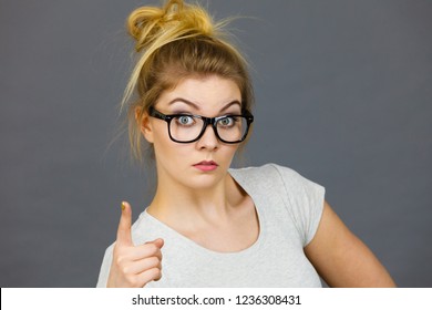 Young Attractive Woman Wearing Eyeglasses Pointing Into Camera, Teenage Judging Someone. Studio Shot On Grey Background.