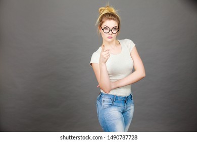 Young Attractive Woman Wearing Eyeglasses Pointing Into Camera, Teenage Judging Someone. Studio Shot On Grey Background.