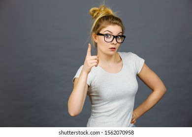 Young Attractive Woman Wearing Eyeglasses Pointing Into Camera, Teenage Judging Someone. Studio Shot On Grey Background.