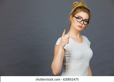 Young Attractive Woman Wearing Eyeglasses Pointing Into Camera, Teenage Judging Someone. Studio Shot On Grey Background.