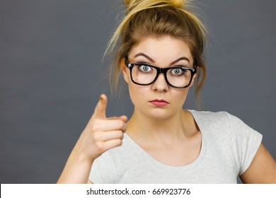 Young Attractive Woman Wearing Eyeglasses Pointing Into Camera, Teenage Judging Someone. Studio Shot On Grey Background.