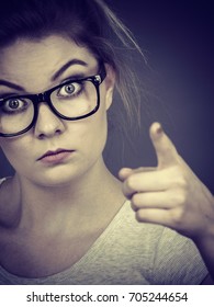 Young Attractive Woman Wearing Eyeglasses Pointing Into Camera, Teenage Judging Someone. Studio Shot On Grey Background.