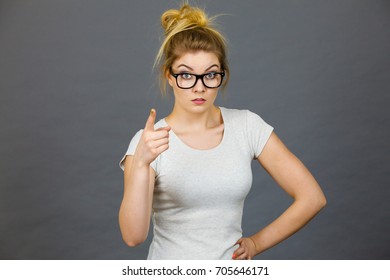 Young Attractive Woman Wearing Eyeglasses Pointing Into Camera, Teenage Judging Someone. Studio Shot On Grey Background.