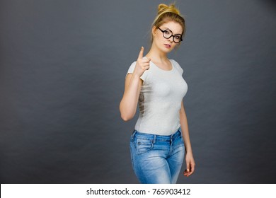 Young Attractive Woman Wearing Eyeglasses Pointing Into Camera, Teenage Judging Someone. Studio Shot On Grey Background.