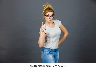 Young Attractive Woman Wearing Eyeglasses Pointing Into Camera, Teenage Judging Someone. Studio Shot On Grey Background.