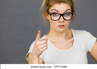 Young Attractive Woman Wearing Eyeglasses Pointing Into Camera, Teenage Judging Someone. Studio Shot On Grey Background.