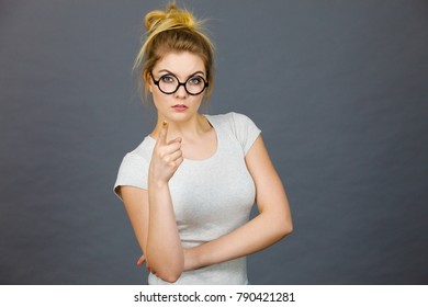 Young Attractive Woman Wearing Eyeglasses Pointing Into Camera, Teenage Judging Someone. Studio Shot On Grey Background.