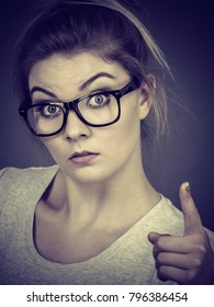 Young Attractive Woman Wearing Eyeglasses Pointing Into Camera, Teenage Judging Someone. Studio Shot On Grey Background.