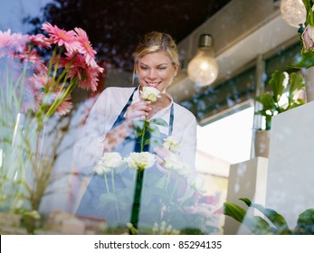 Young attractive woman working in flower shop, preparing bouquet and smelling white roses - Powered by Shutterstock