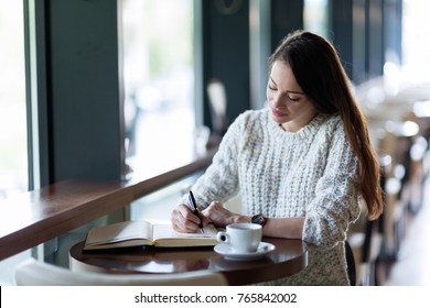 Young Attractive Woman Writing Diary In Cafe