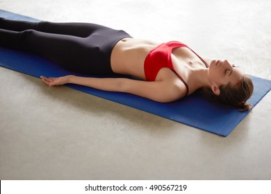 Young Attractive Woman In Yoga Outfit Rests On The Floor Of The Gym Room In Savasana Corpse Pose After Yoga Class