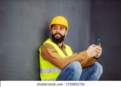 Young attractive worker crouching in working wear crouching and using smart phone on lunch break.