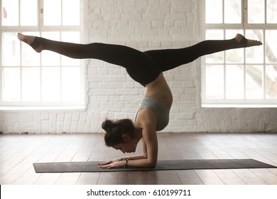 Young attractive yogi woman practicing yoga concept, standing in variation of Pincha Mayurasana exercise, handstand pose, working out, wearing sportswear, full length, white loft studio background  - Shutterstock ID 610199711