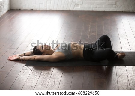 Young attractive yogi woman practicing yoga concept, lying in Reclined Butterfly exercise, supta baddha konasana pose, working out, wearing sportswear, full length, white loft studio background