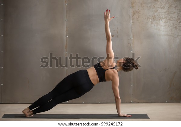 Young attractive yogi woman practicing yoga,\
standing in Side Plank exercise, Vasisthasana pose, working out,\
wearing black sportswear, cool urban style, full length, grey\
studio background, rear\
view