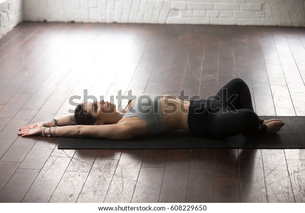Young attractive yogi woman practicing yoga\
concept, lying in Reclined Butterfly exercise, supta baddha\
konasana pose, working out, wearing sportswear, full length, white\
loft studio background