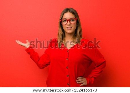 Young authentic charismatic real people woman against a wall showing a copy space on a palm and holding another hand on waist.