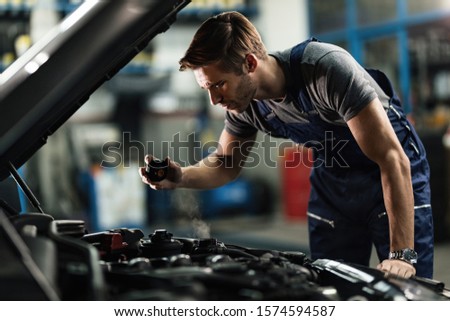 Young auto mechanic checking overheated car coolant system in auto repair shop.